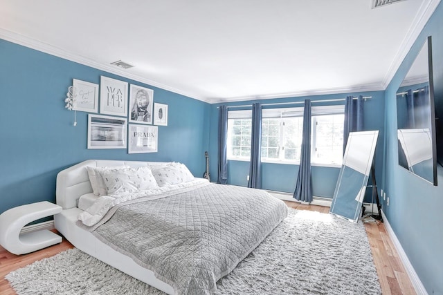 bedroom featuring hardwood / wood-style flooring, crown molding, and a baseboard heating unit