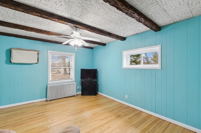 interior space featuring ceiling fan, radiator heating unit, beamed ceiling, and light hardwood / wood-style floors