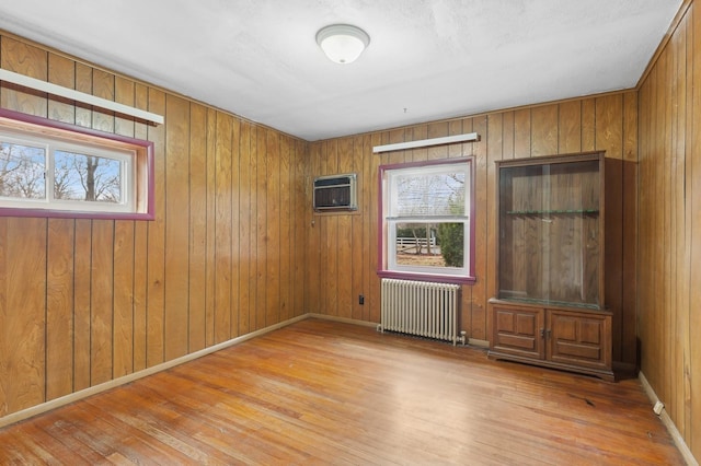 unfurnished room featuring light hardwood / wood-style floors, wood walls, radiator heating unit, and a wall unit AC