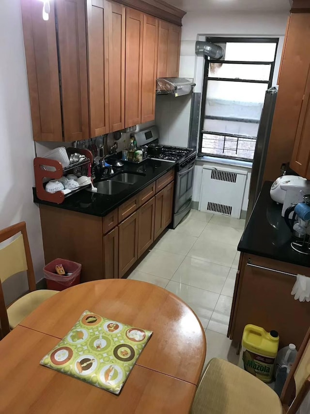 kitchen featuring radiator, sink, stainless steel gas range oven, range hood, and light tile patterned floors