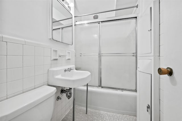 full bathroom with tile patterned flooring, toilet, bath / shower combo with glass door, and tile walls