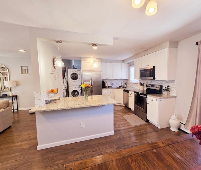 kitchen featuring appliances with stainless steel finishes, dark hardwood / wood-style flooring, stacked washing maching and dryer, white cabinets, and hanging light fixtures