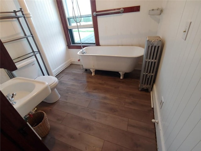 bathroom featuring radiator, a bath, wood-type flooring, toilet, and wooden walls