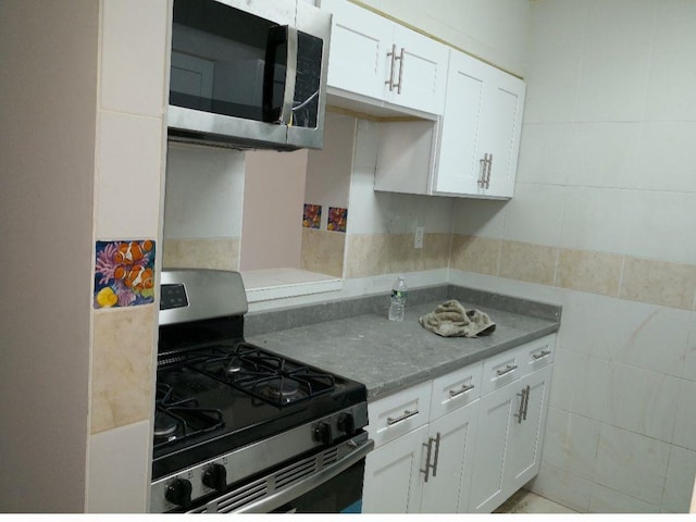 kitchen with white cabinets, appliances with stainless steel finishes, and tile walls