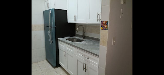 kitchen featuring white cabinets, light stone countertops, black refrigerator, and sink