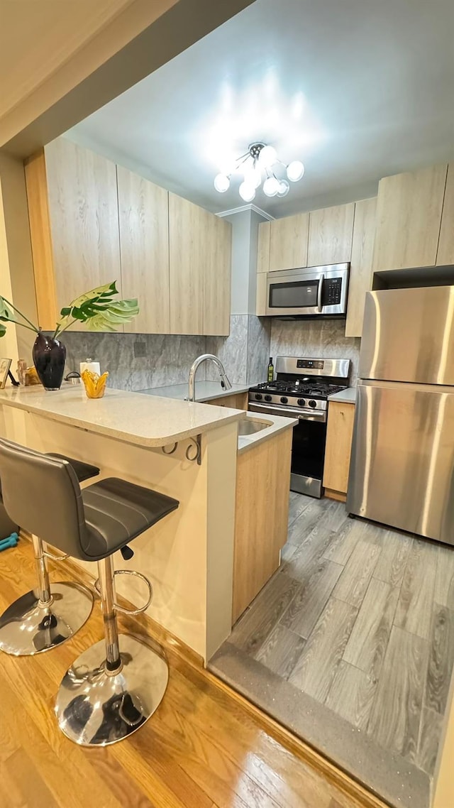 kitchen with light brown cabinets, stainless steel appliances, kitchen peninsula, light hardwood / wood-style flooring, and a breakfast bar area