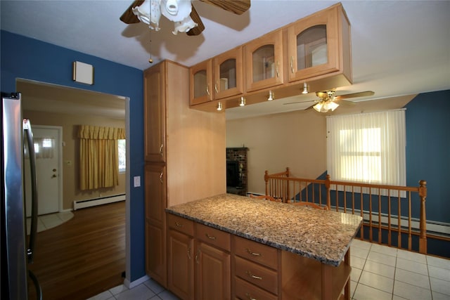 kitchen with kitchen peninsula, stainless steel fridge, light stone counters, and a baseboard heating unit