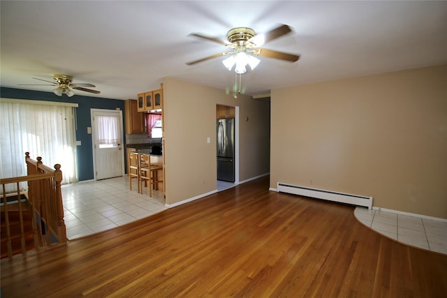 unfurnished living room with ceiling fan, light hardwood / wood-style floors, and a baseboard heating unit