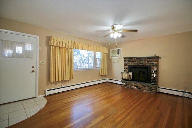 unfurnished living room with a wall unit AC, baseboard heating, ceiling fan, hardwood / wood-style flooring, and a fireplace