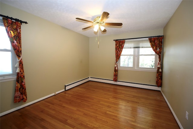 unfurnished room featuring baseboard heating, a wealth of natural light, and hardwood / wood-style flooring