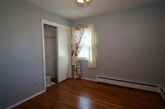 unfurnished bedroom featuring a baseboard heating unit, a closet, dark wood-type flooring, and ceiling fan