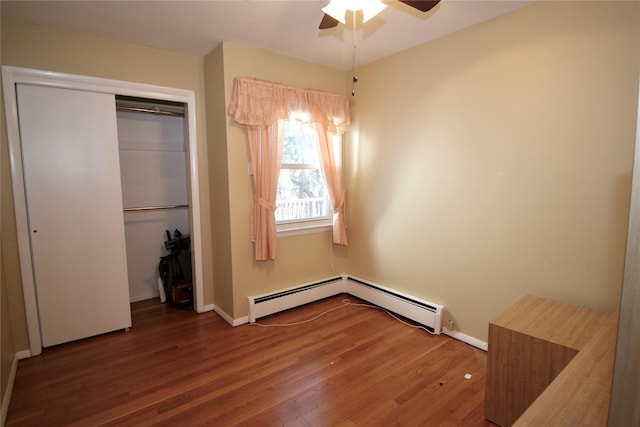 unfurnished bedroom with dark hardwood / wood-style flooring, a closet, a baseboard heating unit, and ceiling fan