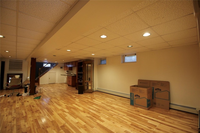 basement with a paneled ceiling, light hardwood / wood-style flooring, and a baseboard heating unit