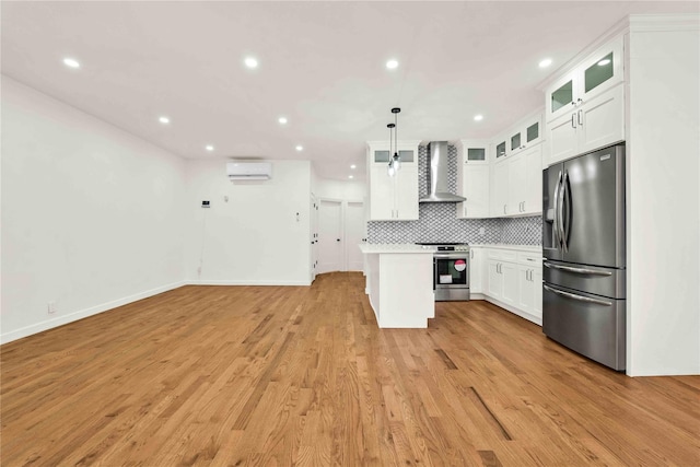 kitchen featuring appliances with stainless steel finishes, wall chimney range hood, pendant lighting, light hardwood / wood-style flooring, and white cabinetry