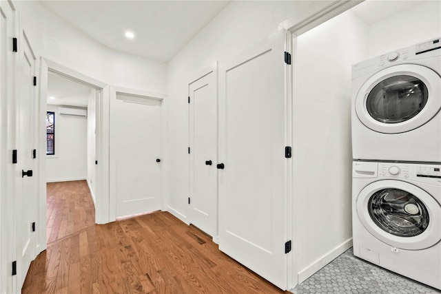 laundry room featuring an AC wall unit, stacked washer / dryer, and light hardwood / wood-style flooring