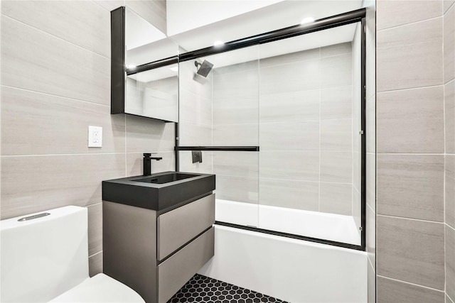 full bathroom with combined bath / shower with glass door, tile patterned floors, vanity, tile walls, and toilet