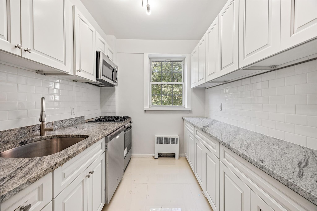 kitchen featuring white cabinets, appliances with stainless steel finishes, radiator heating unit, and sink