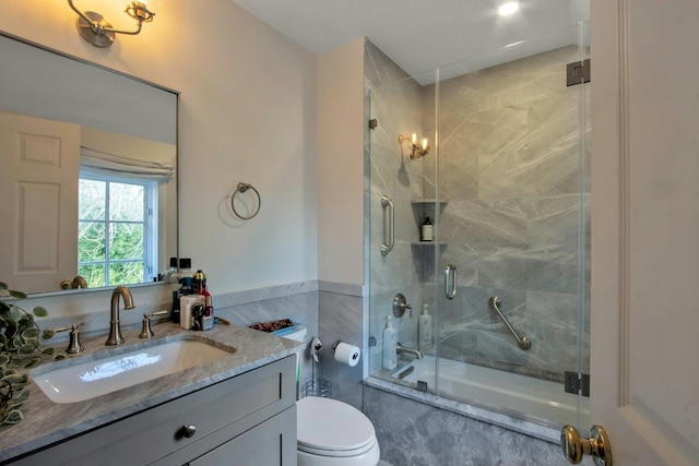 full bathroom featuring vanity, toilet, tile walls, and bath / shower combo with glass door