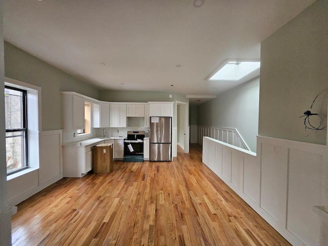 kitchen with appliances with stainless steel finishes, a skylight, sink, light hardwood / wood-style flooring, and white cabinets