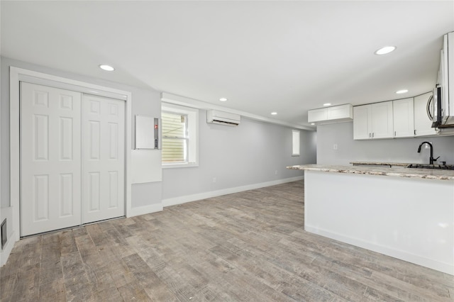 kitchen featuring light stone counters, white cabinets, a wall mounted air conditioner, and light wood-type flooring