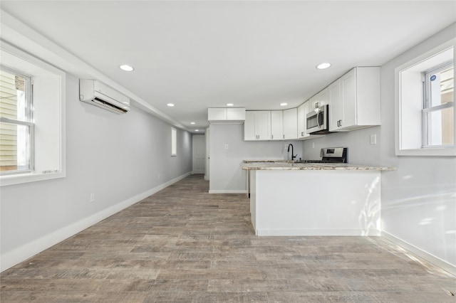 kitchen with light stone counters, stainless steel appliances, a wall mounted AC, white cabinets, and light hardwood / wood-style floors