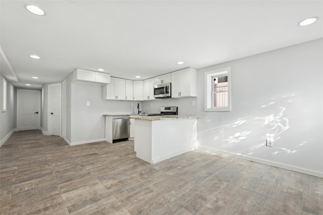 kitchen featuring kitchen peninsula, light stone counters, stainless steel appliances, light hardwood / wood-style floors, and white cabinetry