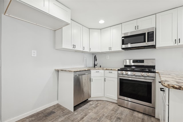 kitchen with sink, light hardwood / wood-style flooring, light stone countertops, white cabinetry, and stainless steel appliances