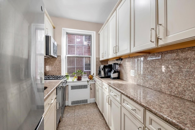 kitchen with tasteful backsplash, light stone countertops, radiator heating unit, and appliances with stainless steel finishes