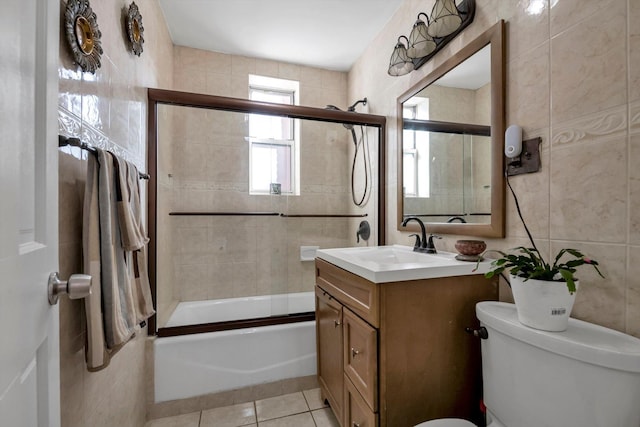 full bathroom featuring tile patterned flooring, toilet, shower / bath combination with glass door, vanity, and tile walls