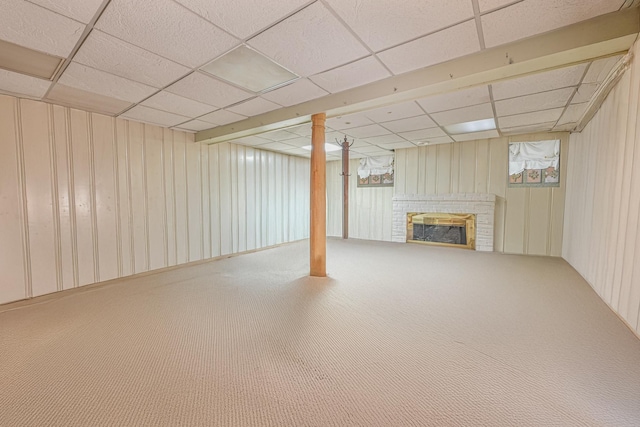 basement with carpet flooring, a paneled ceiling, wood walls, and a fireplace