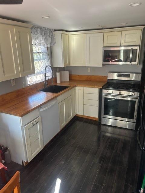 kitchen featuring dark wood-style flooring, wooden counters, appliances with stainless steel finishes, white cabinets, and a sink