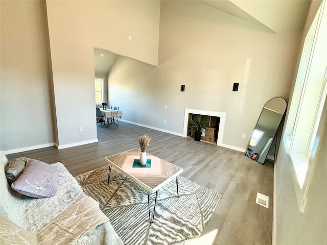 living area with a high ceiling, a fireplace, wood finished floors, and visible vents