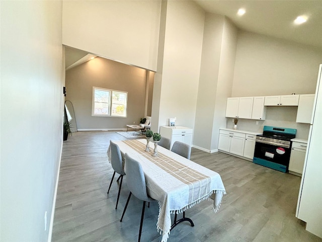 dining space featuring high vaulted ceiling, light wood-style floors, and baseboards