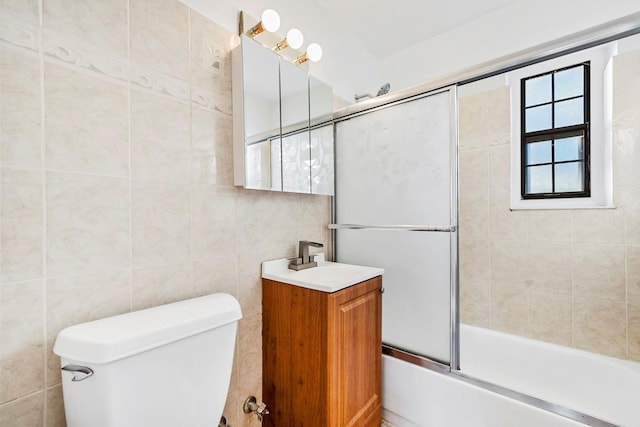 full bathroom featuring toilet, vanity, tile walls, and combined bath / shower with glass door