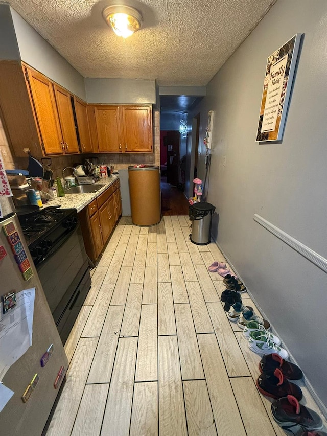 kitchen featuring a textured ceiling, gas stove, sink, and light hardwood / wood-style flooring