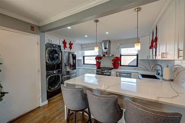 kitchen featuring stainless steel appliances, light stone counters, kitchen peninsula, island exhaust hood, and stacked washer and clothes dryer