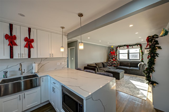 kitchen featuring kitchen peninsula, white cabinetry, stainless steel microwave, and sink