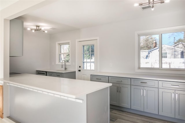 kitchen with an inviting chandelier, kitchen peninsula, gray cabinets, dark hardwood / wood-style flooring, and sink