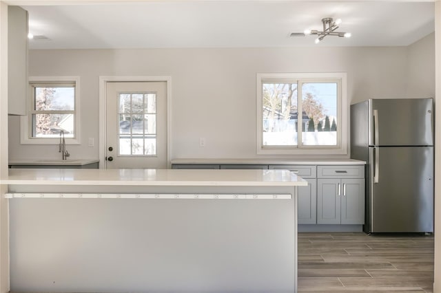 kitchen with stainless steel fridge, sink, gray cabinetry, and a notable chandelier