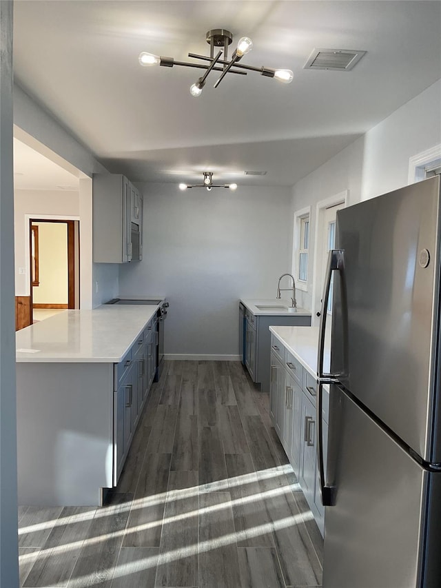 kitchen featuring kitchen peninsula, sink, an inviting chandelier, dark wood-type flooring, and stainless steel fridge