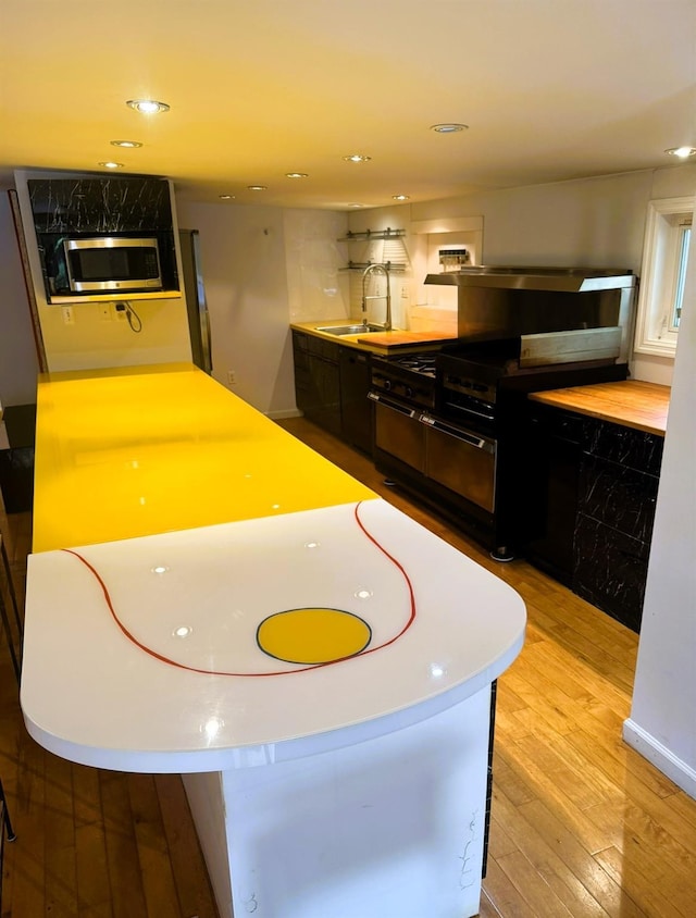 kitchen with black gas range oven, sink, and light hardwood / wood-style flooring