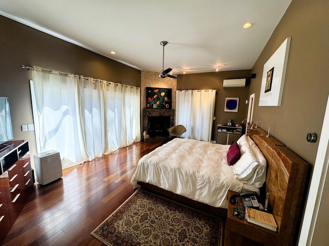 bedroom featuring a large fireplace, an AC wall unit, and dark wood-type flooring