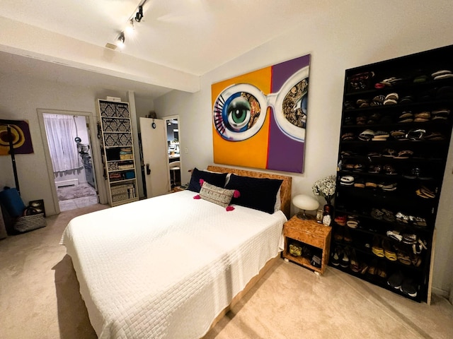 bedroom featuring beamed ceiling, track lighting, light colored carpet, and ensuite bath