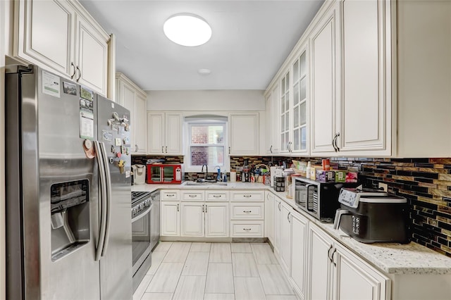 kitchen with light stone countertops, sink, decorative backsplash, white cabinets, and appliances with stainless steel finishes