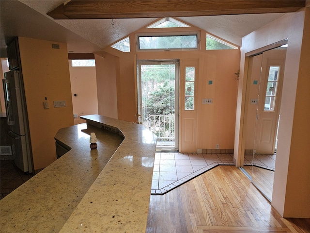 entryway with lofted ceiling with beams, light wood-type flooring, and a textured ceiling