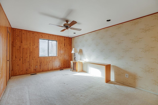 spare room featuring ceiling fan, light carpet, wood walls, and ornamental molding