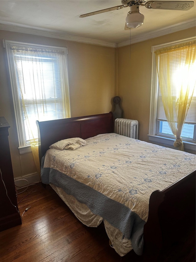 bedroom featuring ceiling fan, radiator heating unit, dark wood-type flooring, and multiple windows