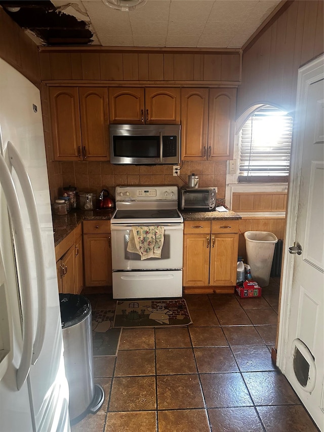 kitchen featuring decorative backsplash, white appliances, wooden walls, crown molding, and dark tile patterned flooring