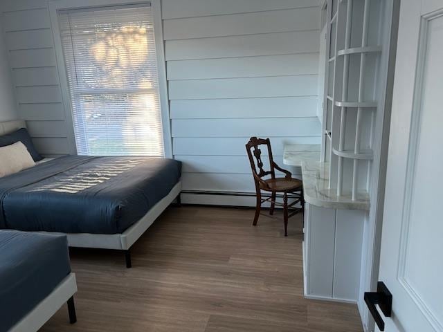 bedroom featuring wood-type flooring, baseboard heating, and wooden walls