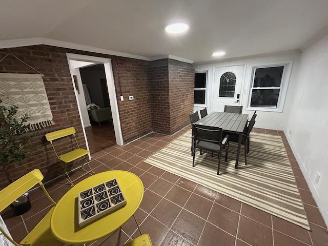 dining space featuring dark tile patterned flooring and brick wall